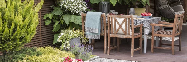 Panorama of wooden chairs at table with apples on terrace with flowers