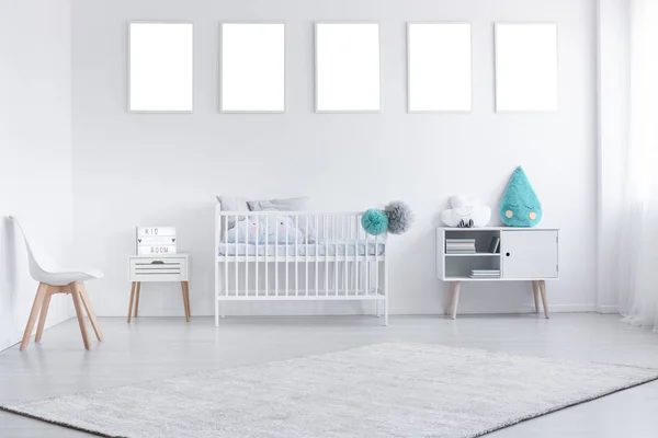 Mockup of empty posters above cradle in white baby's room interior with chair and carpet. Real photo