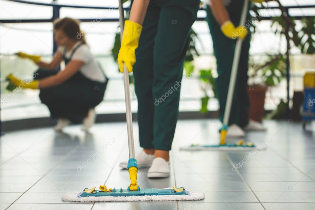 Close-up on cleaning specialist with yellow gloves holding mop while wiping floor