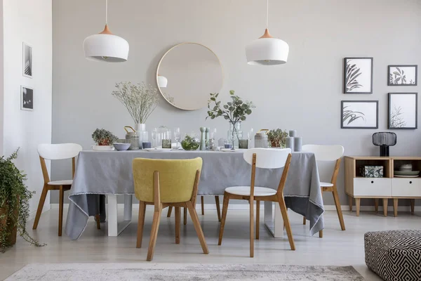 Real photo of an elegant dining room interior with a laid table, chairs, mirror on a wall and lamps