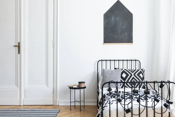 ドアやテーブルに単純なベッドルームのインテリアでベッドの上の白い壁に黒のポスター 実際の写真 — ストック写真