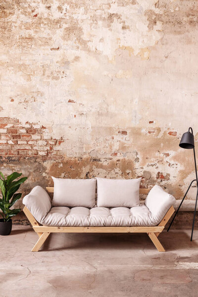 Grey wooden sofa between plant and black lamp in minimal loft interior with red brick wall. Real photo