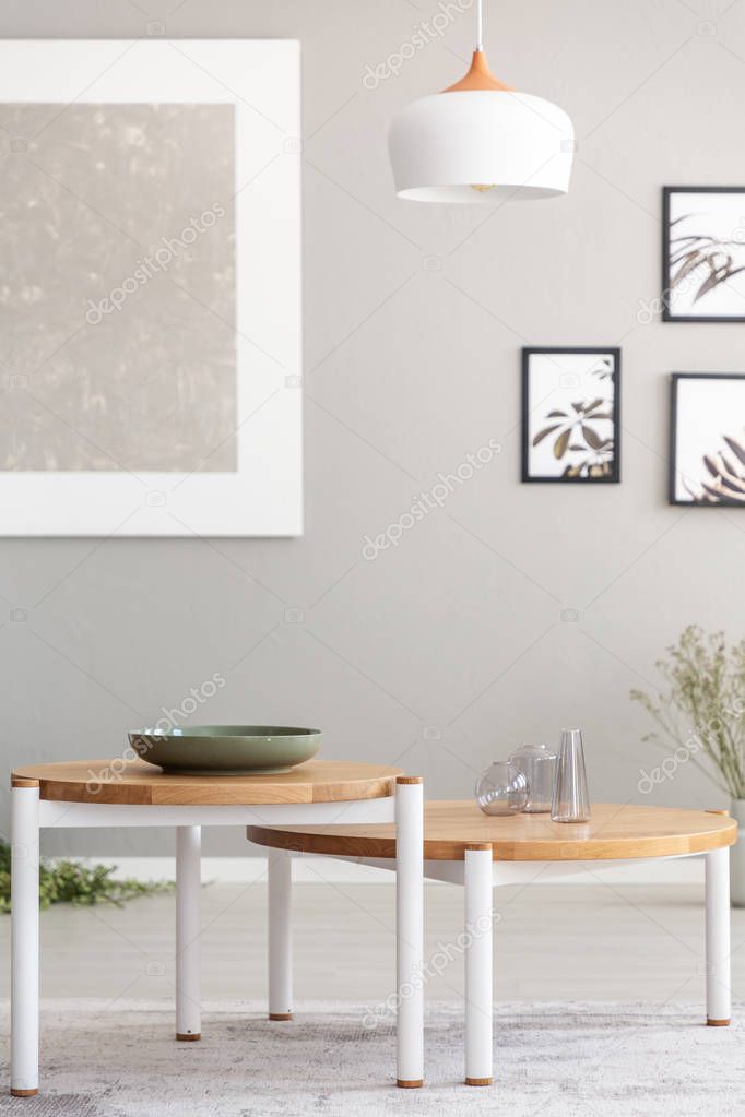 Lamp above wooden tables in grey living room interior with posters and mockup. Real photo