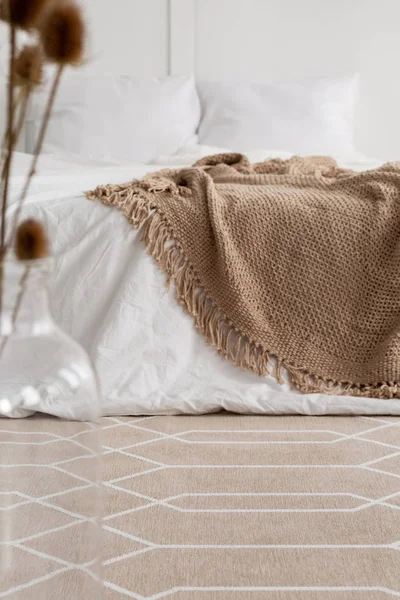 Patterned carpet in natural bedroom interior with brown blanket on white bed. Real photo