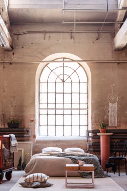 Real photo of an arch window in a wabi sabi bedroom interior with a bed, raw walls and table clipart