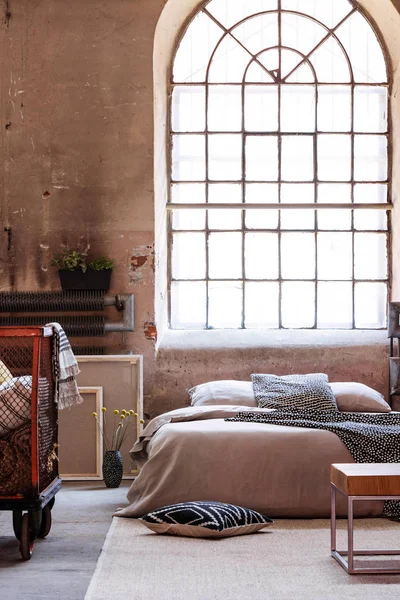 Real photo of an industrial bedroom interior with a big window and double bed