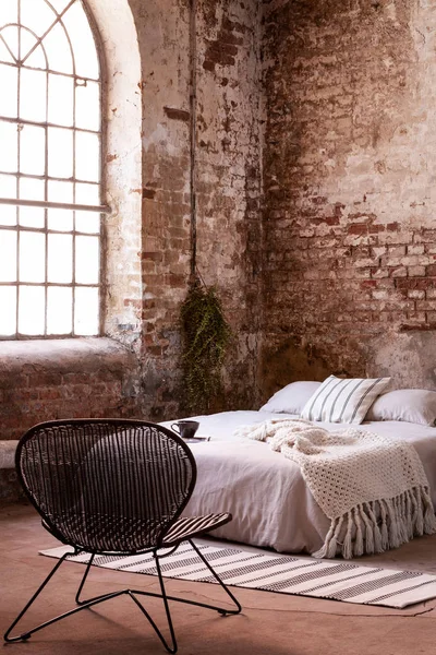 Raw wall in an industrial bedroom interior with a bed and armchair. Real photo