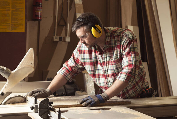 Worker in protective glasses and headphones cutting wood in a sawmill