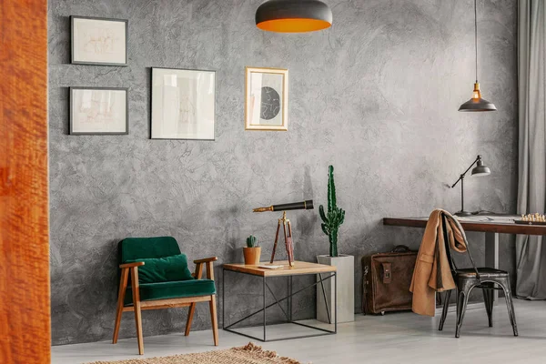 Living room interior with posters on raw grey wall, green retro armchair, end table with telescope and cactus in the real photo