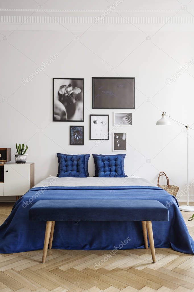 Photo gallery on a white wall above a navy blue bed with elegant cushions in a stylish bedroom interior with herringbone parquet floor
