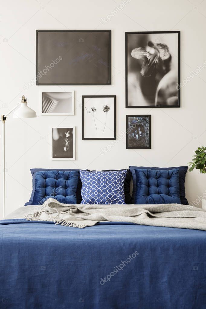 Mock-up picture gallery on a white wall above a large bed with navy blue bedding in a bright and modern bedroom interior