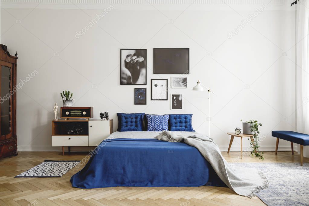 Vintage bedroom interior with bedside table, king size bed with blue bedding and pillows. Mockup gallery on the white wall. Real photo concept