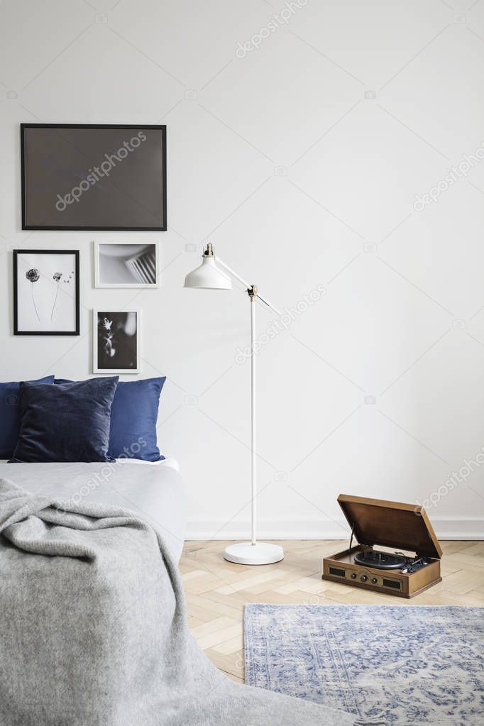 Retro vinyl record player and an industrial style floor lamp in a hipster bedroom interior with framed pictures and copy space