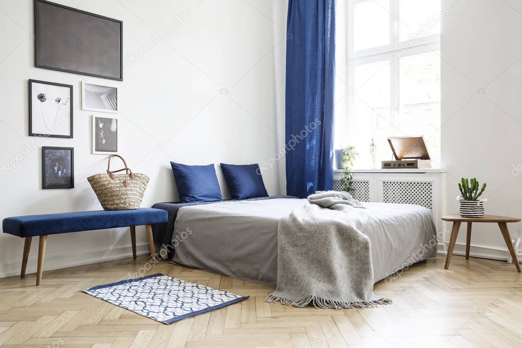 Bedroom design in modern apartment. Bed with dark blue pillows and grey duvet and blanket next to window. Real photo concept
