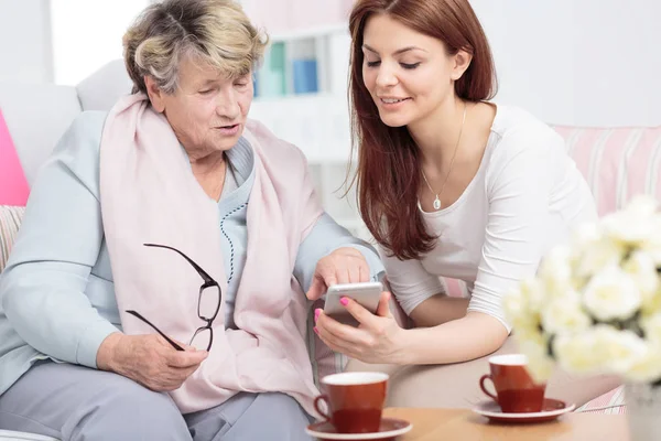 Lächelnde Tochter Zeigt Seniorin Beim Teetrinken Smartphone — Stockfoto