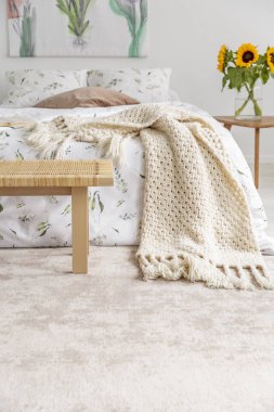 Organik pamuk yaprak ve battaniye ayakta pastel yatak odası iç yumuşak bir halı üzerinde rahat yatak. Yatağın yanındaki masada sarı ayçiçeği. Gerçek fotoğraf.