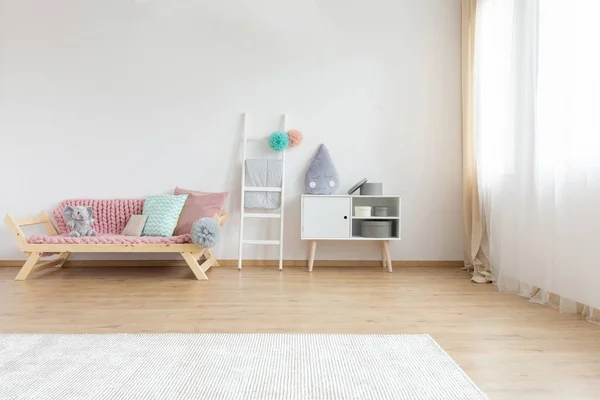 舒适的沙发 粉色毯子和五颜六色的枕头旁边的白色木梯和搁板圆形框 复制空间的白色墙壁和地毯的木地板上 — 图库照片