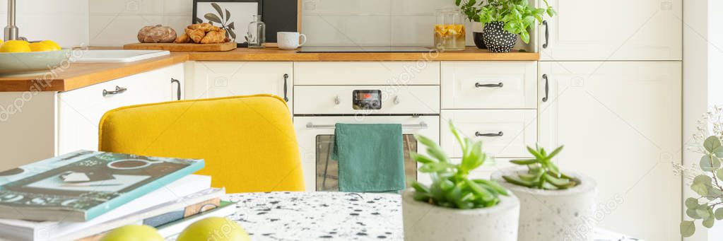 Closeup of stylish kitchen interior design with white cabinets, oven and yellow chair, panoramic view, real photo