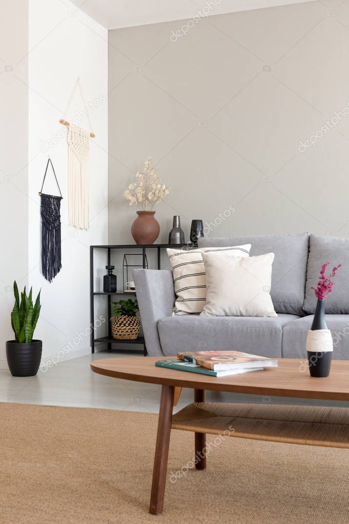 Flowers on wooden table in front of grey settee in simple living room interior with plant. Real photo