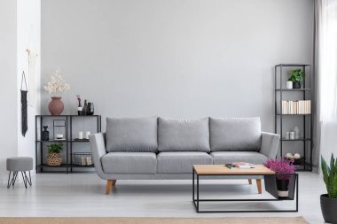 Modern daire basit iç dışkı ile gri kanepe önünde ahşap masa çiçeklenir. Gerçek fotoğraf