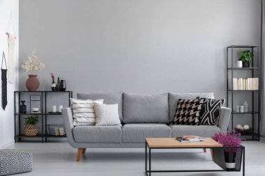 Kitap, mumlar ve bitki gri koltuk kopya alanı Duvar ile gerçek fotoğraf ile desenli yastıklar, arkasında siyah metal raflar