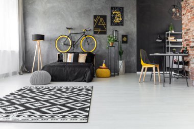 Desenli halı ve posterler gri yatak odası iç lamba yakınındaki siyah yatak üzerinde bisiklet ile. Gerçek fotoğraf