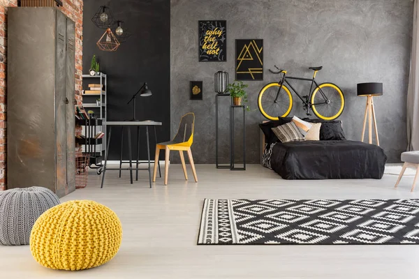 灰色青少年房间的黄色脚凳和图案地毯 上面有自行车 上面有黑色的床 真实照片 — 图库照片