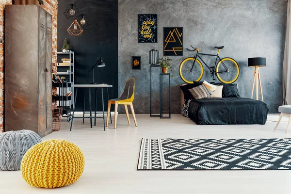 灰色卧室内有图案地毯和黄色脚凳 黑色床上有自行车 真实照片 — 图库照片