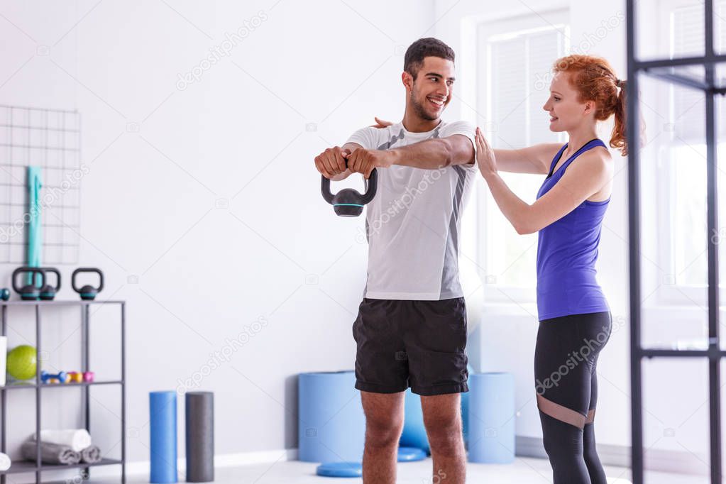 Smiling personal trainer and sportswoman working out with weight at gym