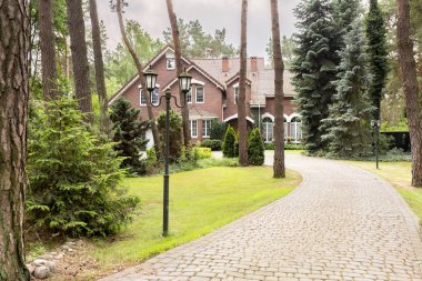 A long cobbled driveway in woods leading to an English style house. clipart