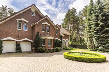 Arnavut kaldırımlı daire driveway dik çatı ve beyaz windows geleneksel kırmızı tuğla İngilizce evin önünde yeşil çalılar dekorasyon ile.