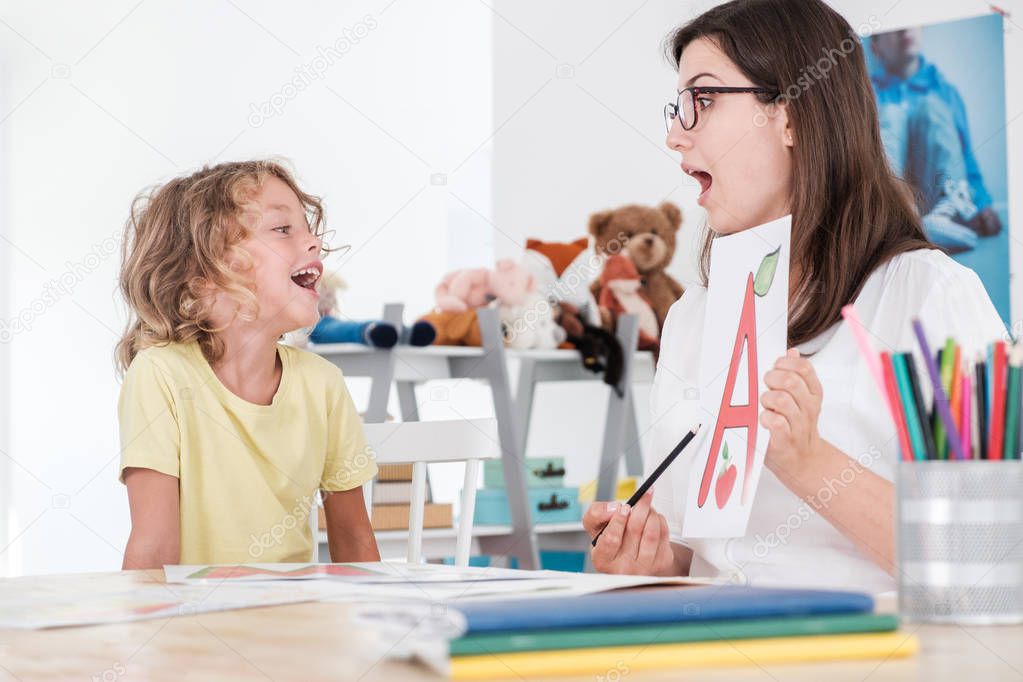 A happy child pronouncing a letter during speech therapy with a specialist.