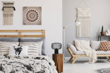 Sıcak etno yatak odası ile yatak ve kanepe desenli yastıklar ve makrome duvar, gerçek bir fotoğraf