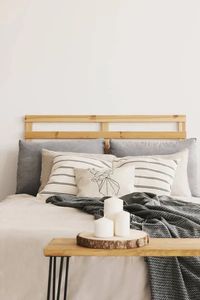 パターン化された枕灰色毛布 壁にコピー スペースを持つ本物の写真と居心地の良いベッドの横に木製のテーブルの つのキャンドル — ストック写真