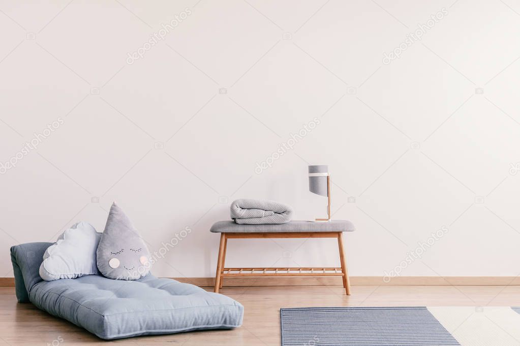 Futon with cute pillows on the floor of stylish baby room interior with copy space on the empty white wall