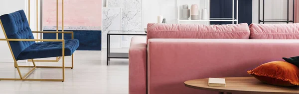 木茶几的全景 配有书籍和枕头旁边的粉粉色沙发在客厅内部与地图 绘画和汽油蓝色长椅 真实的照片 — 图库照片