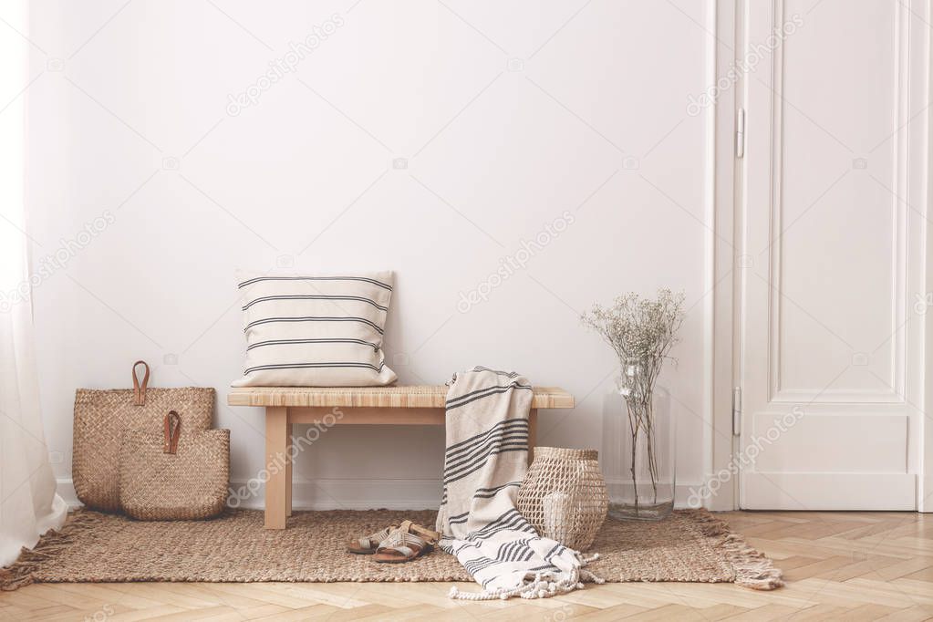 Two bags made of straw next to wooden table with striped pillow and a blanket on it