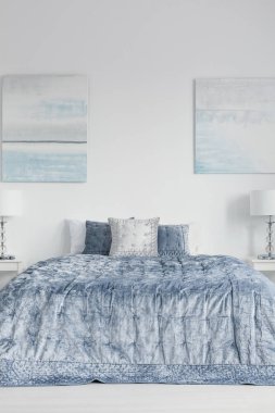 Mavi çarşaf ve yastık yatak odası iç lambalar ile yatak üzerinde beyaz duvar afişlerde. Gerçek fotoğraf