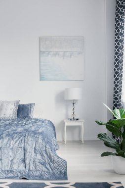 Poster lamba mavi beyaz basit yatak odası iç üretim tesisi ile yatakta yanında dolapla yukarıda. Gerçek fotoğraf