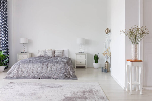 Дизайн интерьера в роскошной спальне с серебристым одеялом и подушками на двуспальной кровати, реальное фото с копировальным пространством
