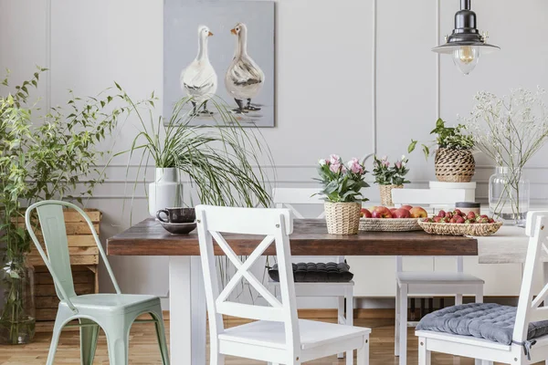 Rustic dining room with long table and white chairs and oil painting on the grey wall, real photo