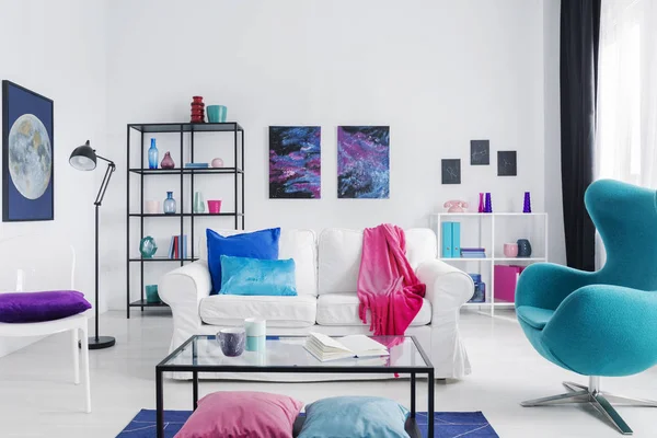 Eclectic living room with blue egg chair, metal coffee table and white couch with colorful pillows, real photo with copy space