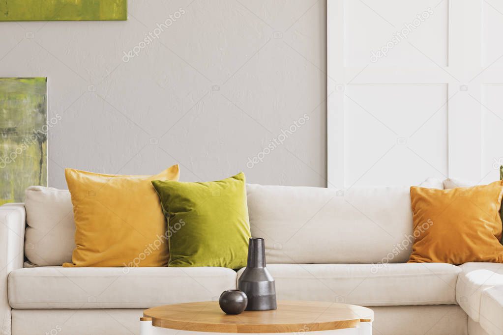 Yellow and green cushion on white settee in simple living room interior with wooden table. Real photo