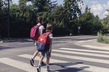 Erkek ve kız okula yaya geçidi üzerinde yürüyen sırt çantaları ile