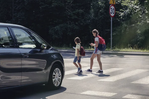 汽车在孩子们面前从学校走出来 看着他们的智能手机 人行横道上 — 图库照片