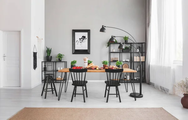 ダイニング テーブル ランプと灰色の壁にポスターとアパート インテリアで食品と黒の椅子 実際の写真 — ストック写真