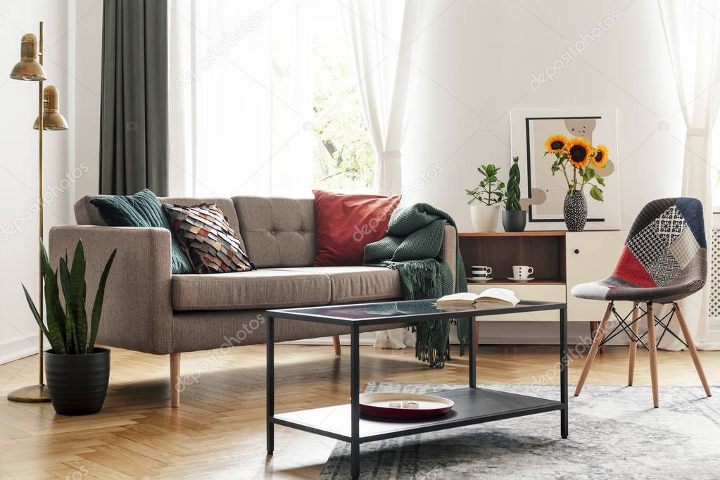 Table in front of chair and sofa in living room interior with sunflowers and gold lamp. Real photo