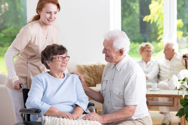 Lachende Ouderen Man Bezoekende Senior Vrouw Rolstoel Terwijl Verpleegkundige Ondersteuning — Stockfoto