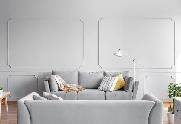 灯旁边的灰色沙发与枕头和毯子在平坦的内部与墙壁与成型 真实照片 — 图库照片
