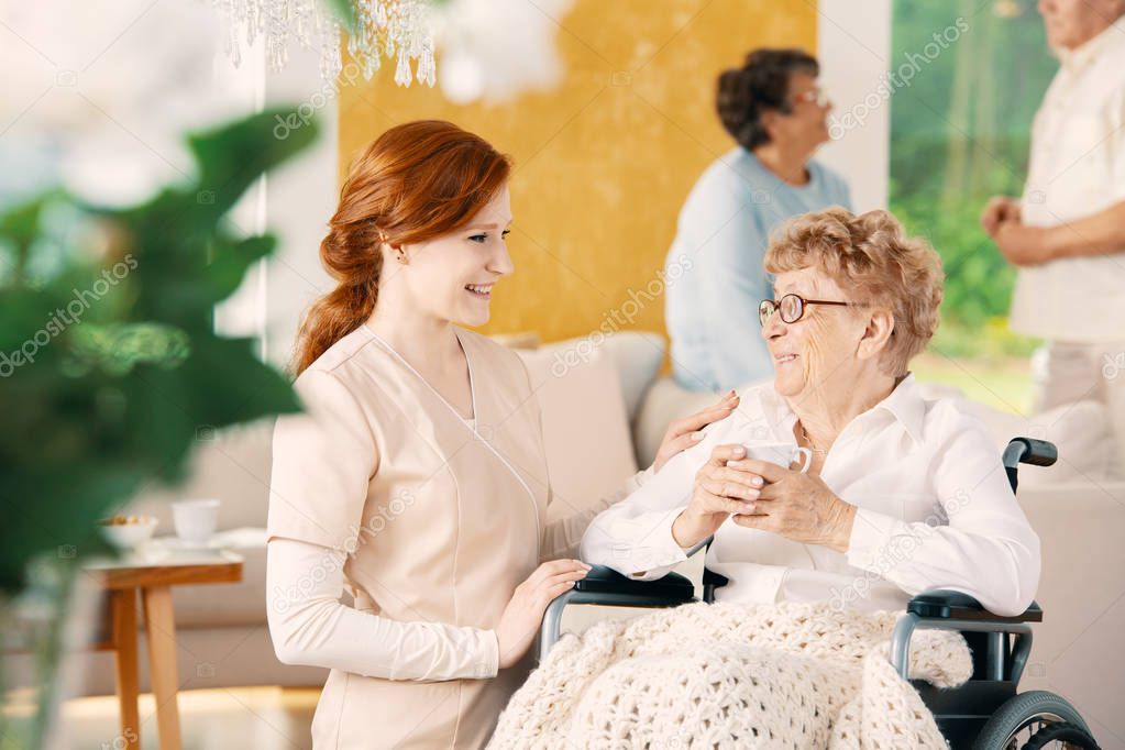 Smiling caregiver supporting disabled senior woman in the wheelchair